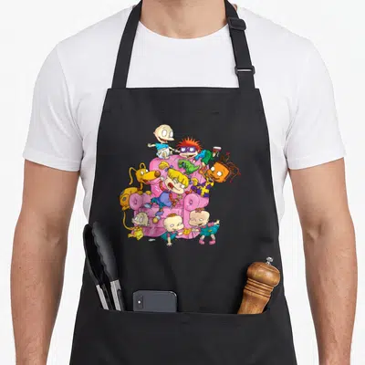 Having couch apron - Cartoon babies and dog climbing a pink armchair in pink yellow blue and green — shown on a black cotton canvas apron against a white background