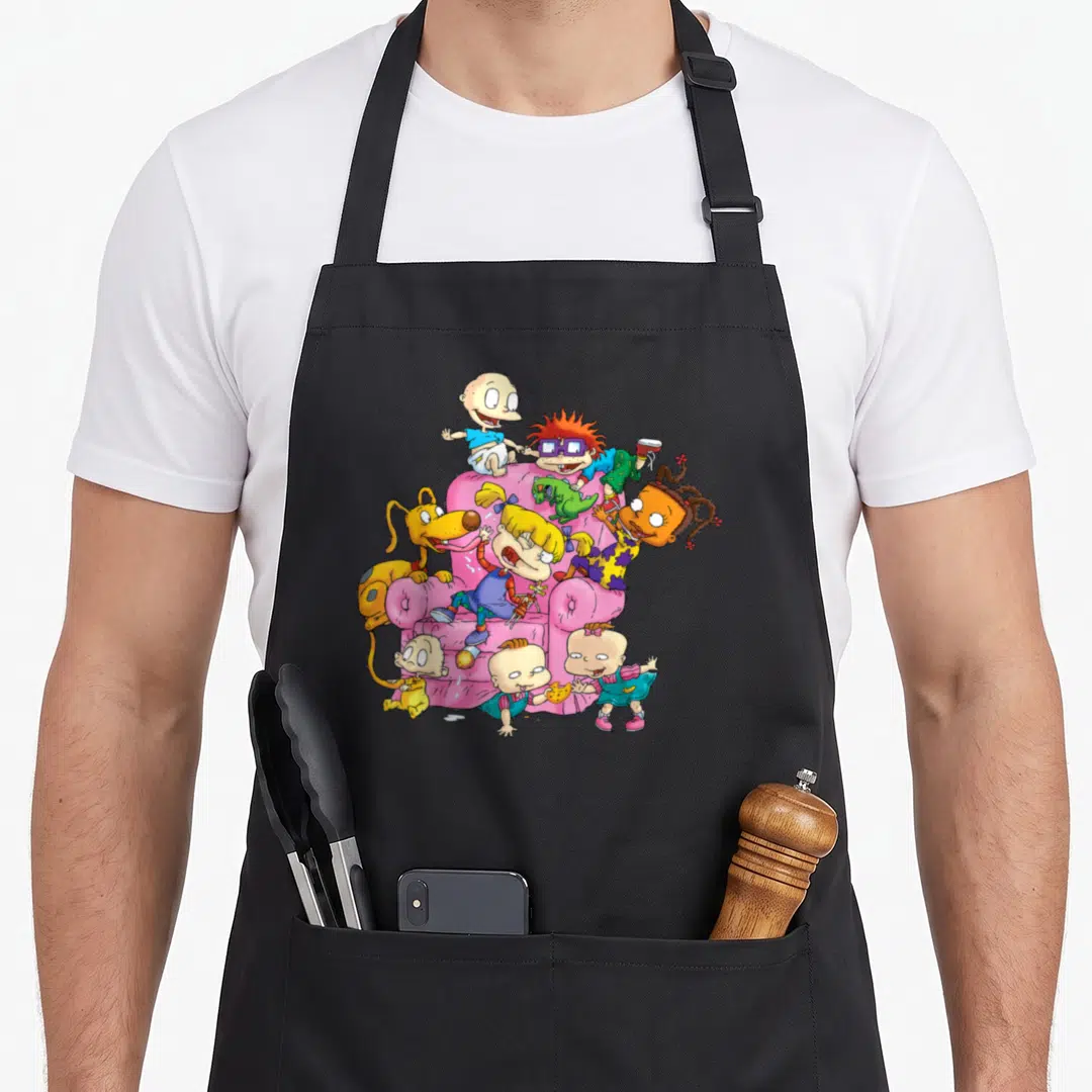 Having couch apron - Cartoon babies and dog climbing a pink armchair in pink yellow blue and green — shown on a black cotton canvas apron against a white background