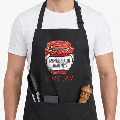 Support mental health awareness apron - Red jam jar with plaid lid, white ribbon, text MENTAL HEALTH AWARENESS IS MY JAM — shown on a black cotton canvas apron against a white background