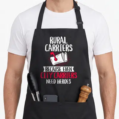 Carrier mail postal aprons - Rural Carriers Because Even City Carriers Need Heroes text with white mailbox and red flag — shown on a black cotton canvas apron against a white background