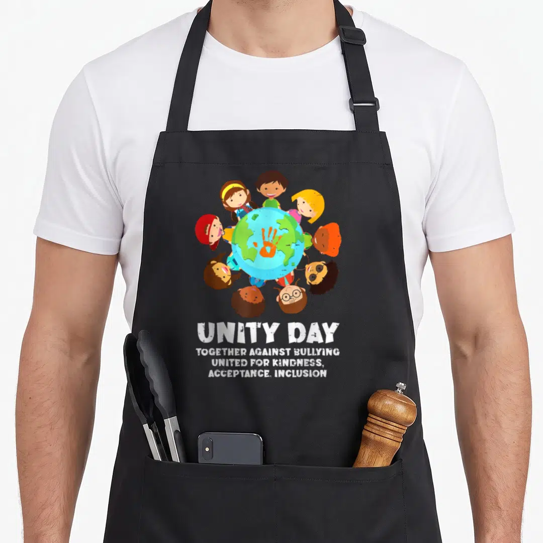 Together unity apron - Ten cartoon children circle a globe with an orange handprint and stacked white anti-bullying text — shown on a black cotton canvas apron against a white background
