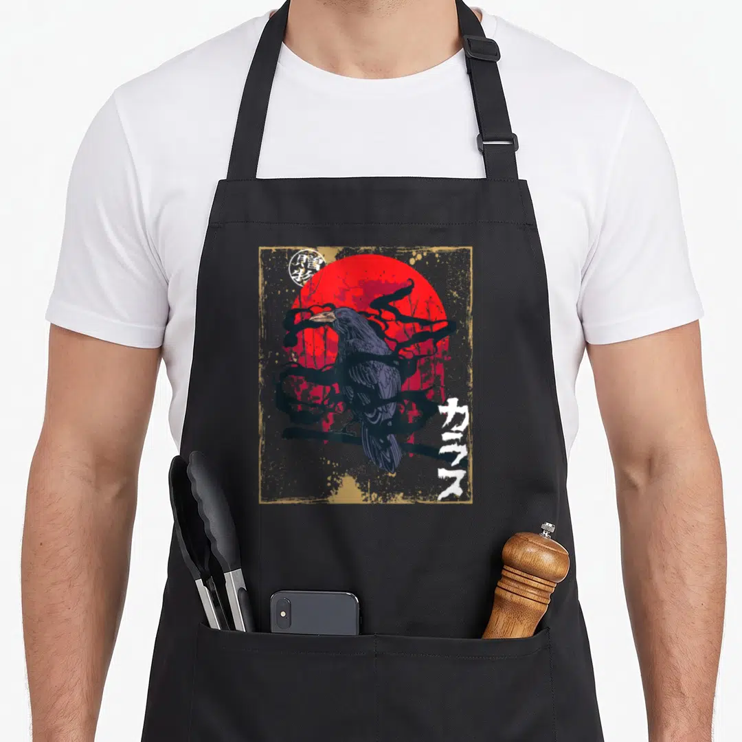 Raven moon gothic apron - Crow perched on branch before red sun with Japanese text and gold border — shown on a black cotton canvas apron against a white background