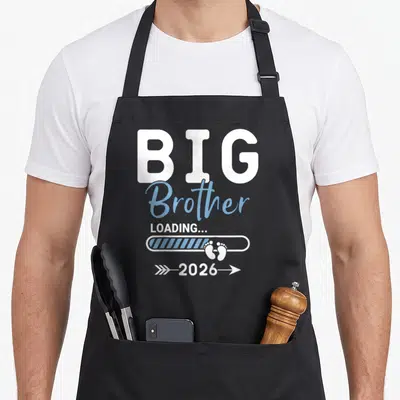 Loading brother apron - White and blue Big Brother Loading 2026 text with baby footprints in a progress bar — shown on a black cotton canvas apron against a white background