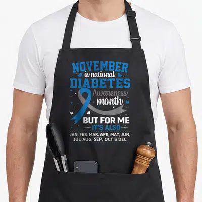 November ribbon apron - Blue ribbon and text listing all twelve months for diabetes awareness — shown on a black cotton canvas apron against a white background