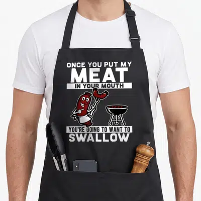 Mouth once you put my meat apron - Sausage character holding fork near grill with bold text pun about meat — shown on a black cotton canvas apron against a white background