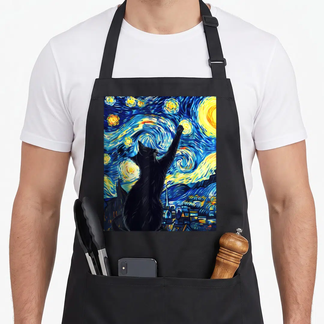 Night cat van gogh apron - Black cat silhouette reaching up at swirling blue and yellow stars above a dark village — shown on a black cotton canvas apron against a white background