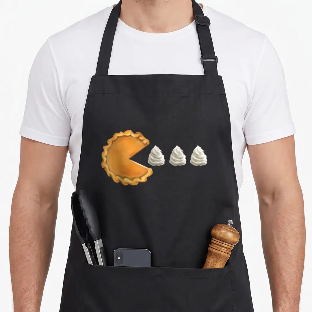 Pumpkin pie apron - Realistic orange pie with missing slice next to three white whipped cream dollops — shown on a black cotton canvas apron against a white background