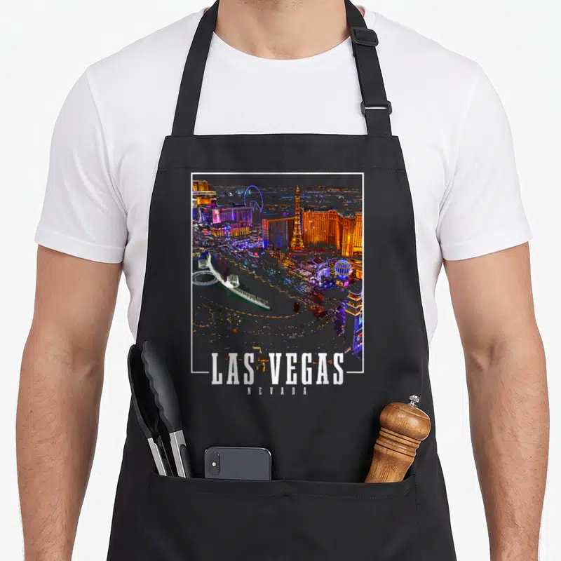 Souvenir las vegas apron - Aerial photo of Las Vegas skyline in orange and blue with white frame and centered text — shown on a black cotton canvas apron against a white background