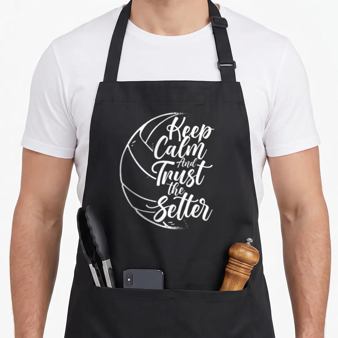 Trust setter apron - White stacked text reading Keep Calm And Trust the Setter inside a volleyball outline — shown on a black cotton canvas apron against a white background