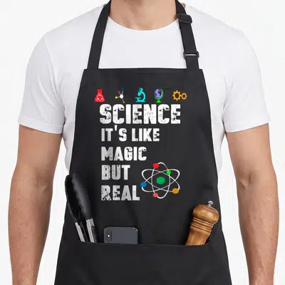 Scientist science apron - Distressed text reading SCIENCE IT'S LIKE MAGIC BUT REAL with lab icons and an atom — shown on a black cotton canvas apron against a white background