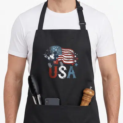 Flute 4th of july apron - Retro Mickey Mouse conducting a waving red white and blue USA flag with musical notes — shown on a black cotton canvas apron against a white background