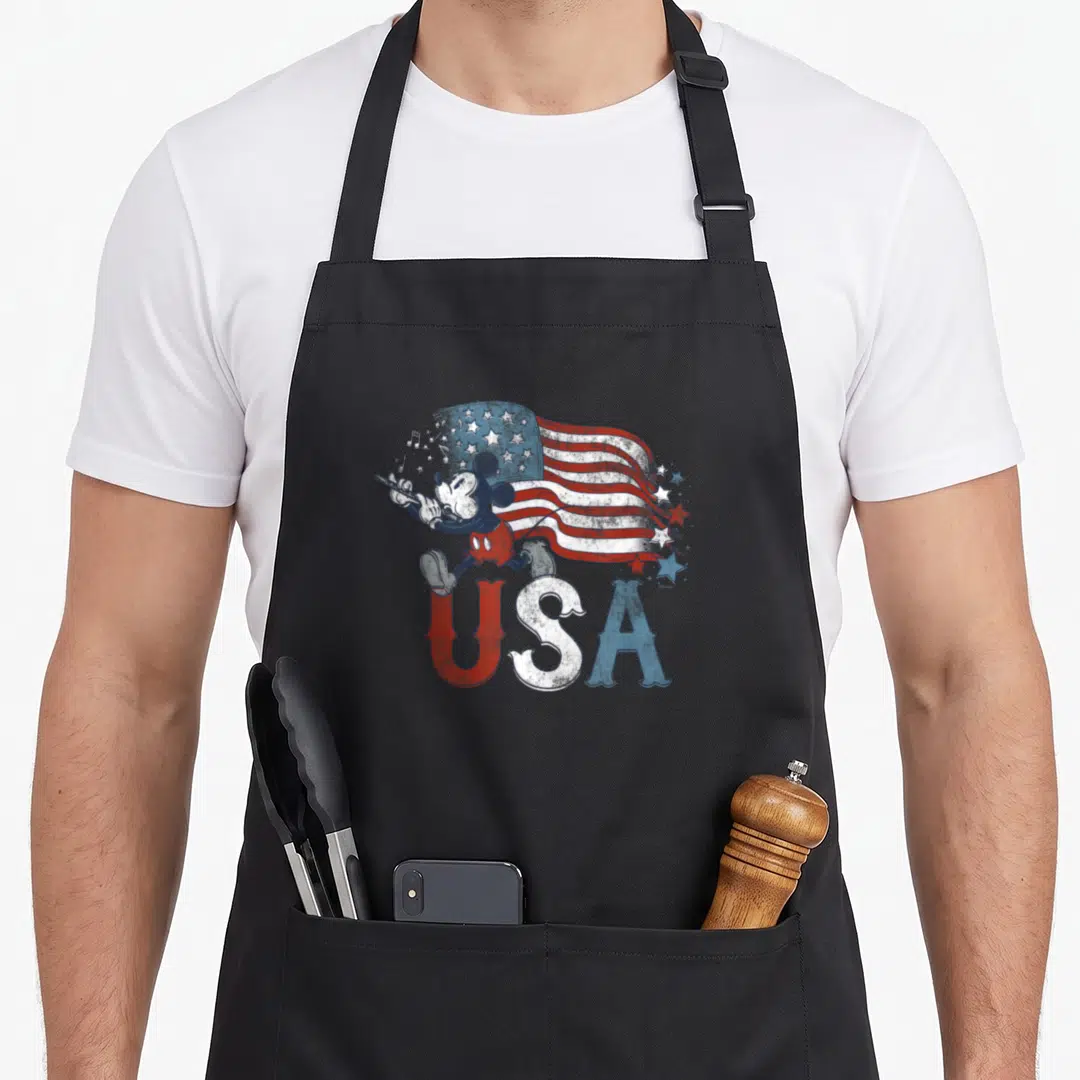 Flute 4th of july apron - Retro Mickey Mouse conducting a waving red white and blue USA flag with musical notes — shown on a black cotton canvas apron against a white background