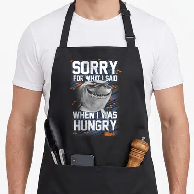 Bruce sorry apron - Realistic grey shark head with white text SORRY FOR WHAT I SAID WHEN I WAS HUNGRY and orange bubbles — shown on a black cotton canvas apron against a white background