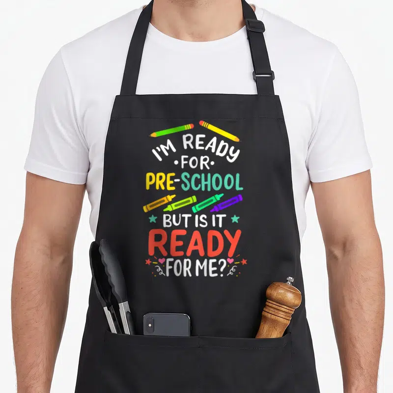 1st preschool apron - Stacked text I'M READY FOR PRE-SCHOOL BUT IS IT READY FOR ME? with pencils, crayons, stars — shown on a black cotton canvas apron against a white background