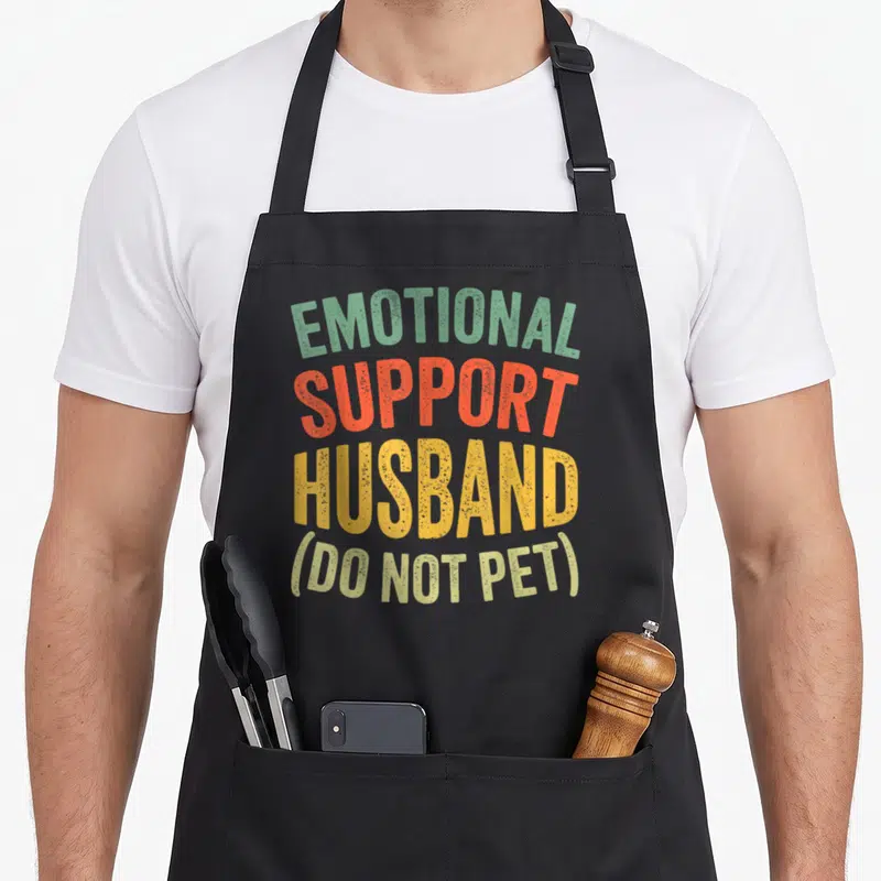 Retro support husband apron - Stacked EMOTIONAL SUPPORT HUSBAND DO NOT PET text in green orange red and yellow — shown on a black cotton canvas apron against a white background