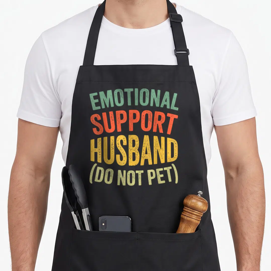 Retro support husband apron - Stacked EMOTIONAL SUPPORT HUSBAND DO NOT PET text in green orange red and yellow — shown on a black cotton canvas apron against a white background