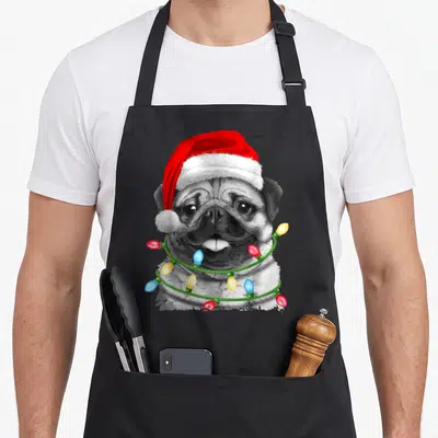 Pugmas christmas tree apron - Realistic pug wearing red Santa hat and wrapped in multicolored Christmas lights — shown on a black cotton canvas apron against a white background