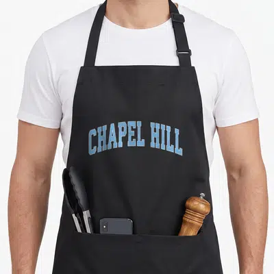 Chapel 80s apron - Arched CHAPEL HILL text in light blue with white outline — shown on a black cotton canvas apron against a white background