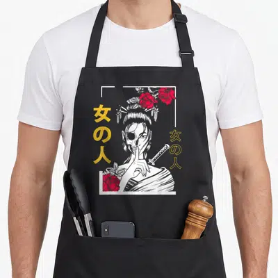 Japanese floral apron - Line-art woman with half-skull face, red roses, and yellow Japanese characters inside white — shown on a black cotton canvas apron against a white background