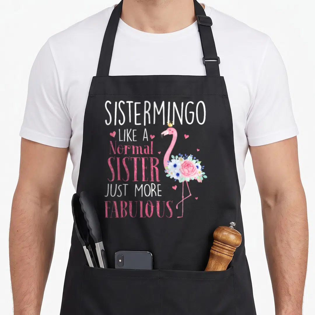 Sistermingo grandma apron - Pink flamingo with gold crown and floral bouquet next to stacked Sistermingo text and hearts — shown on a black cotton canvas apron against a white background
