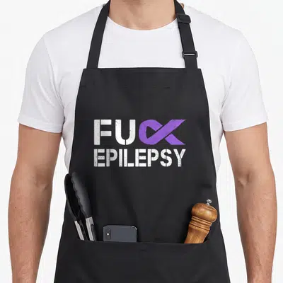 Epilepsy ribbon apron - FUC EPILEPSY text with purple ribbon replacing K in distressed white font — shown on a black cotton canvas apron against a white background