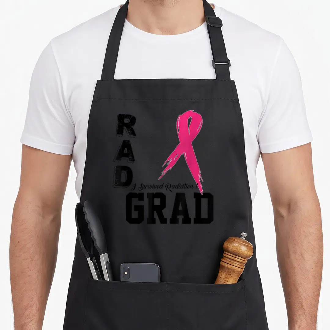 Funny therapy radiation aprons - RAD GRAD text with pink awareness ribbon and I Survived Radiation script in distressed — shown on a black cotton canvas apron against a white background