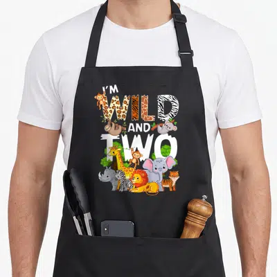 Wild zoo 2nd apron - I'M WILD AND TWO text with cartoon giraffe lion elephant and zebra — shown on a black cotton canvas apron against a white background