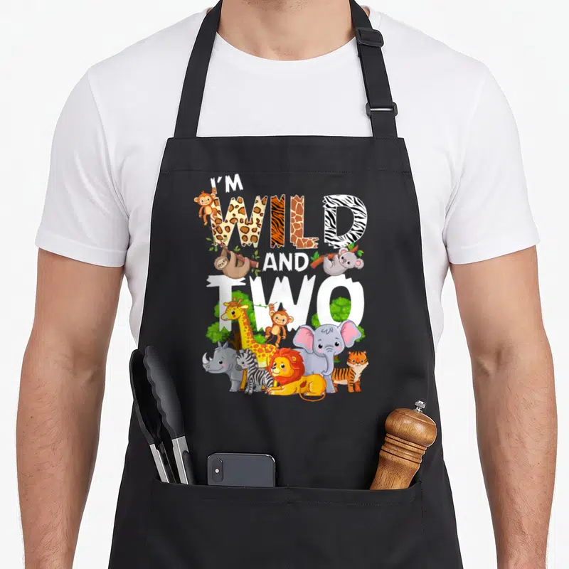 Wild zoo 2nd apron - I'M WILD AND TWO text with cartoon giraffe lion elephant and zebra — shown on a black cotton canvas apron against a white background