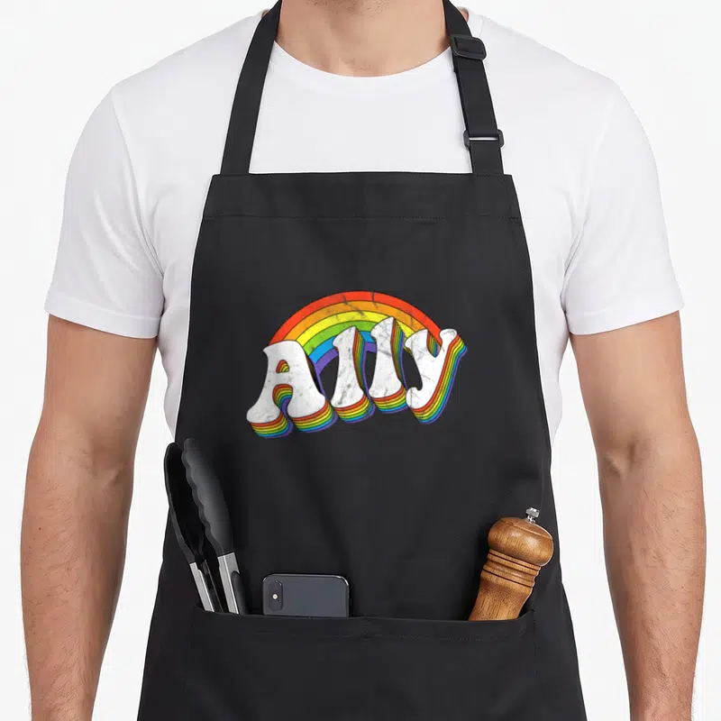 70s gay pride apron - Ally text with 3D rainbow extrusion and arc in red orange yellow green blue purple white — shown on a black cotton canvas apron against a white background