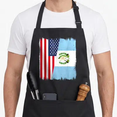 Guatemala guatemalan american flag apron - Split US and Guatemala flag design with distressed edges and LIBERTAD 15 — shown on a black cotton canvas apron against a white background