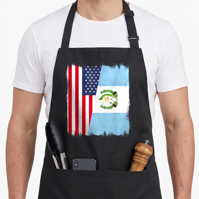 Guatemala guatemalan american flag apron - Split US and Guatemala flag design with distressed edges and LIBERTAD 15 — shown on a black cotton canvas apron against a white background