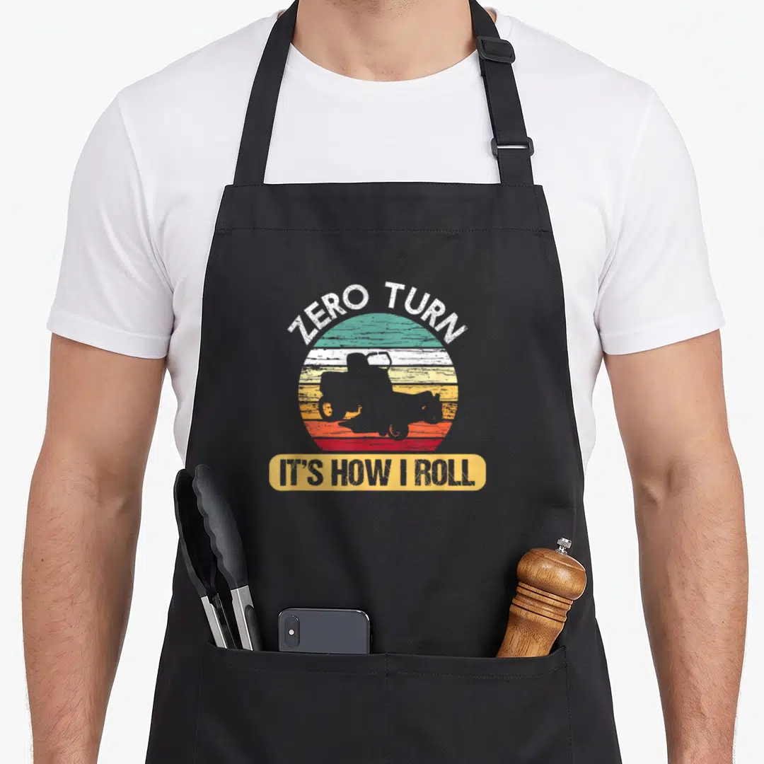Zero mower apron - Retro striped sun with mower silhouette and ZERO TURN IT'S HOW I ROLL text — shown on a black cotton canvas apron against a white background