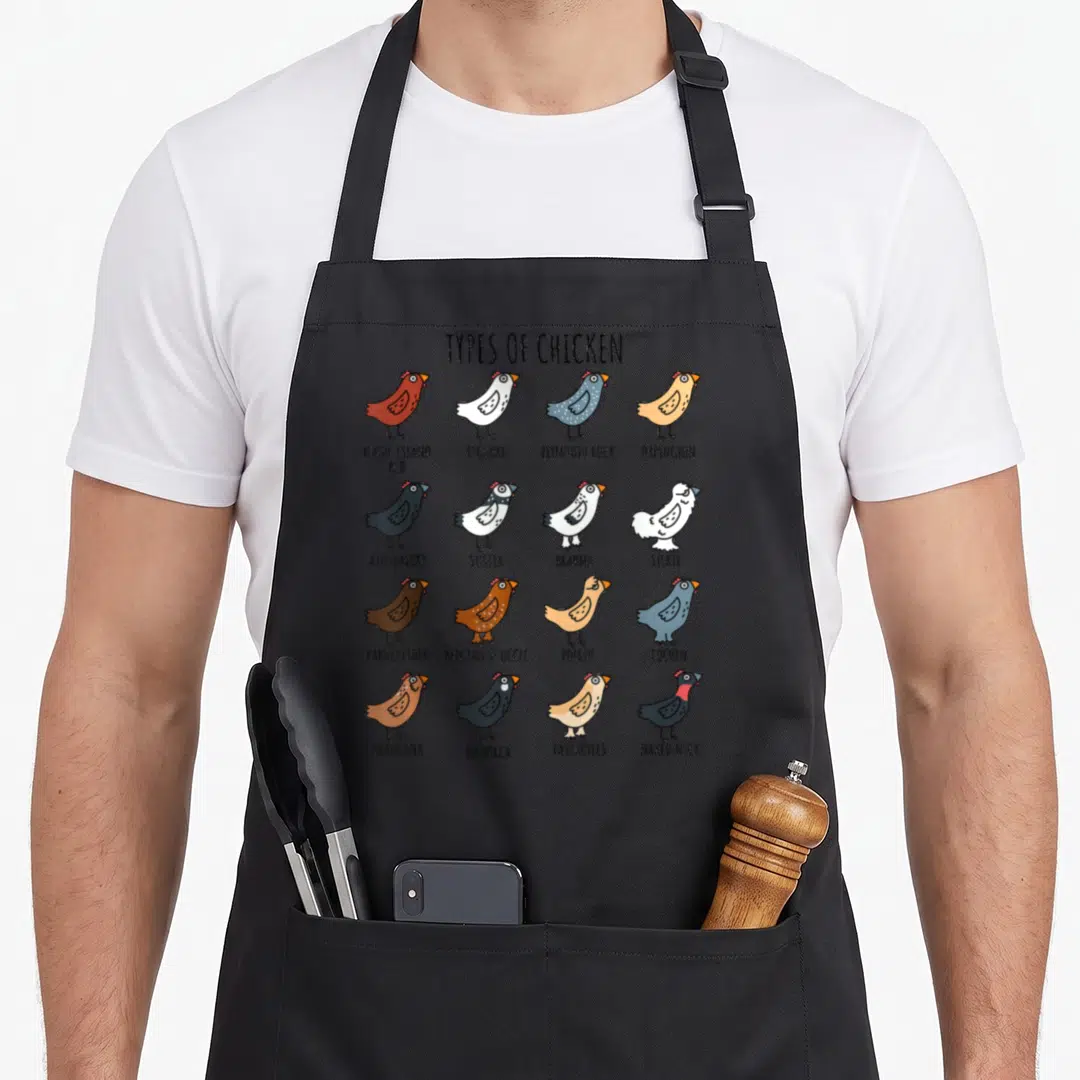 Leghorn chicken with apron - Cartoon grid of 16 chicken breeds including Rhode Island Red, Silkie, and Naked Neck — shown on a black cotton canvas apron against a white background