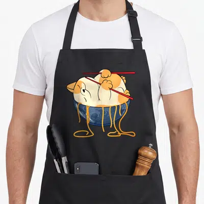 Clothe cat apron - Cartoon orange white cat curled in blue bowl holding red chopsticks with yellow noodles hanging down — shown on a black cotton canvas apron against a white background