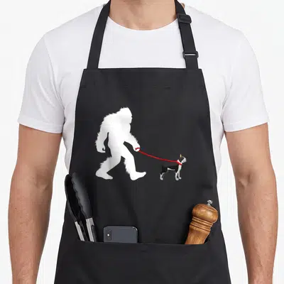 Boston walking apron - White Bigfoot silhouette walking a black and white dog on a red leash — shown on a black cotton canvas apron against a white background