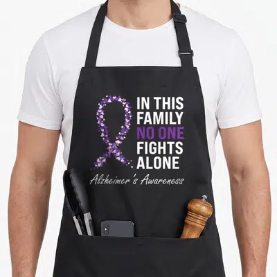 Alzheimer grandpa apron - Purple and white heart ribbon with text In This Family No One Fights Alone Alzheimer's — shown on a black cotton canvas apron against a white background