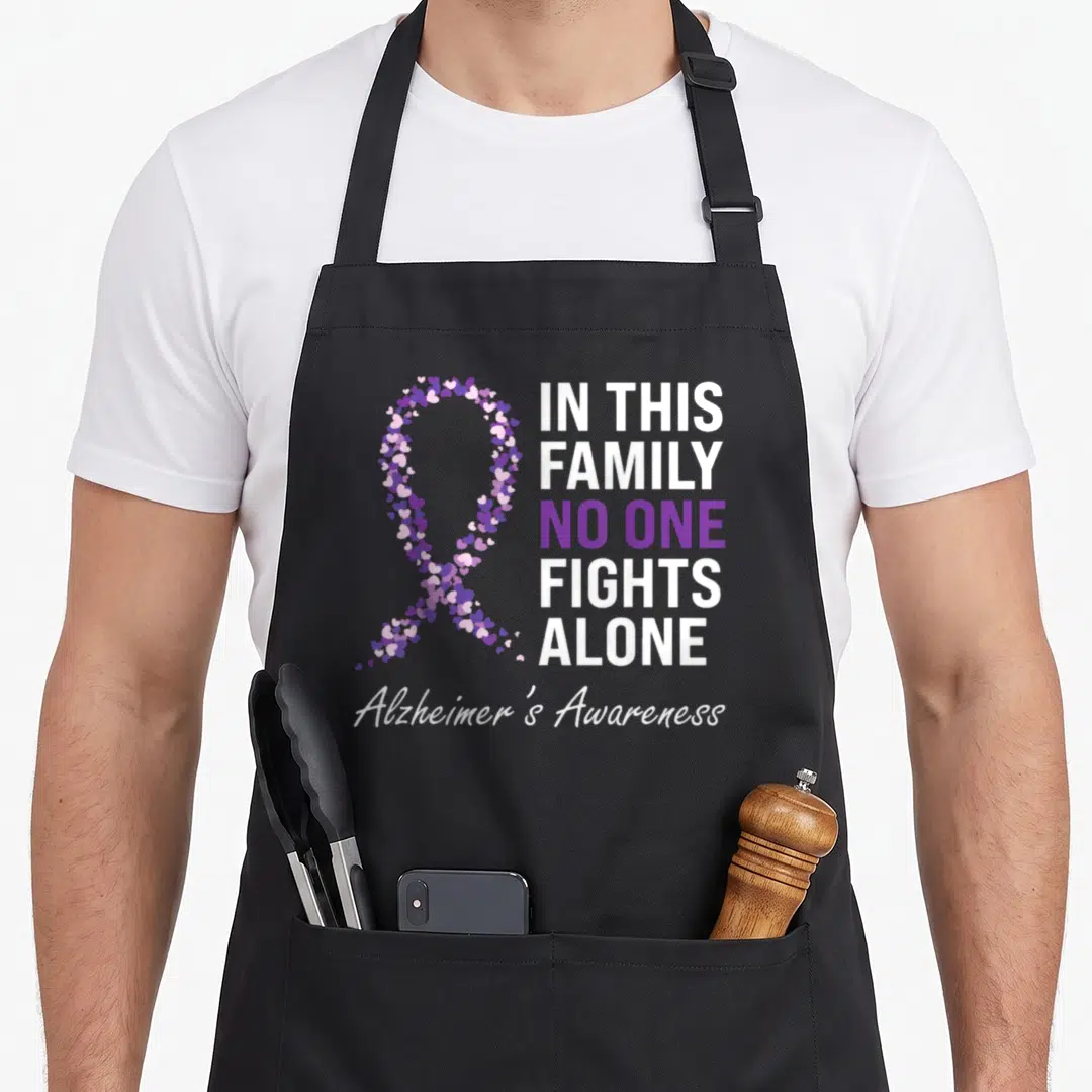 Alzheimer grandpa apron - Purple and white heart ribbon with text In This Family No One Fights Alone Alzheimer's — shown on a black cotton canvas apron against a white background