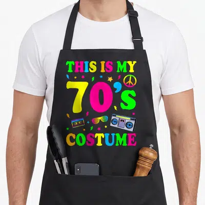 70s halloween apron - Colorful text reading This Is My 70s Costume with boombox, cassette, and peace sign in pink — shown on a black cotton canvas apron against a white background