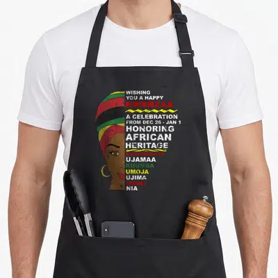 Kwanzaa african apron - Woman in striped turban with Kwanzaa greeting and seven principles text in red green yellow — shown on a black cotton canvas apron against a white background