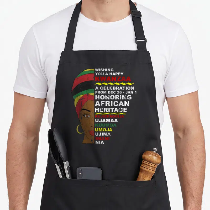Kwanzaa african apron - Woman in striped turban with Kwanzaa greeting and seven principles text in red green yellow — shown on a black cotton canvas apron against a white background