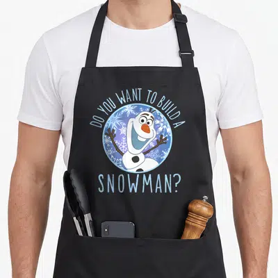 Frozen snowman apron - Olaf snowman in blue circle with DO YOU WANT TO BUILD A SNOWMAN text arched above and below — shown on a black cotton canvas apron against a white background