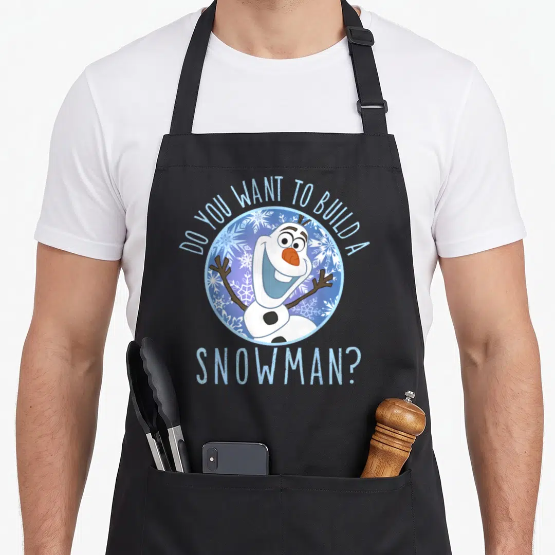 Frozen snowman apron - Olaf snowman in blue circle with DO YOU WANT TO BUILD A SNOWMAN text arched above and below — shown on a black cotton canvas apron against a white background