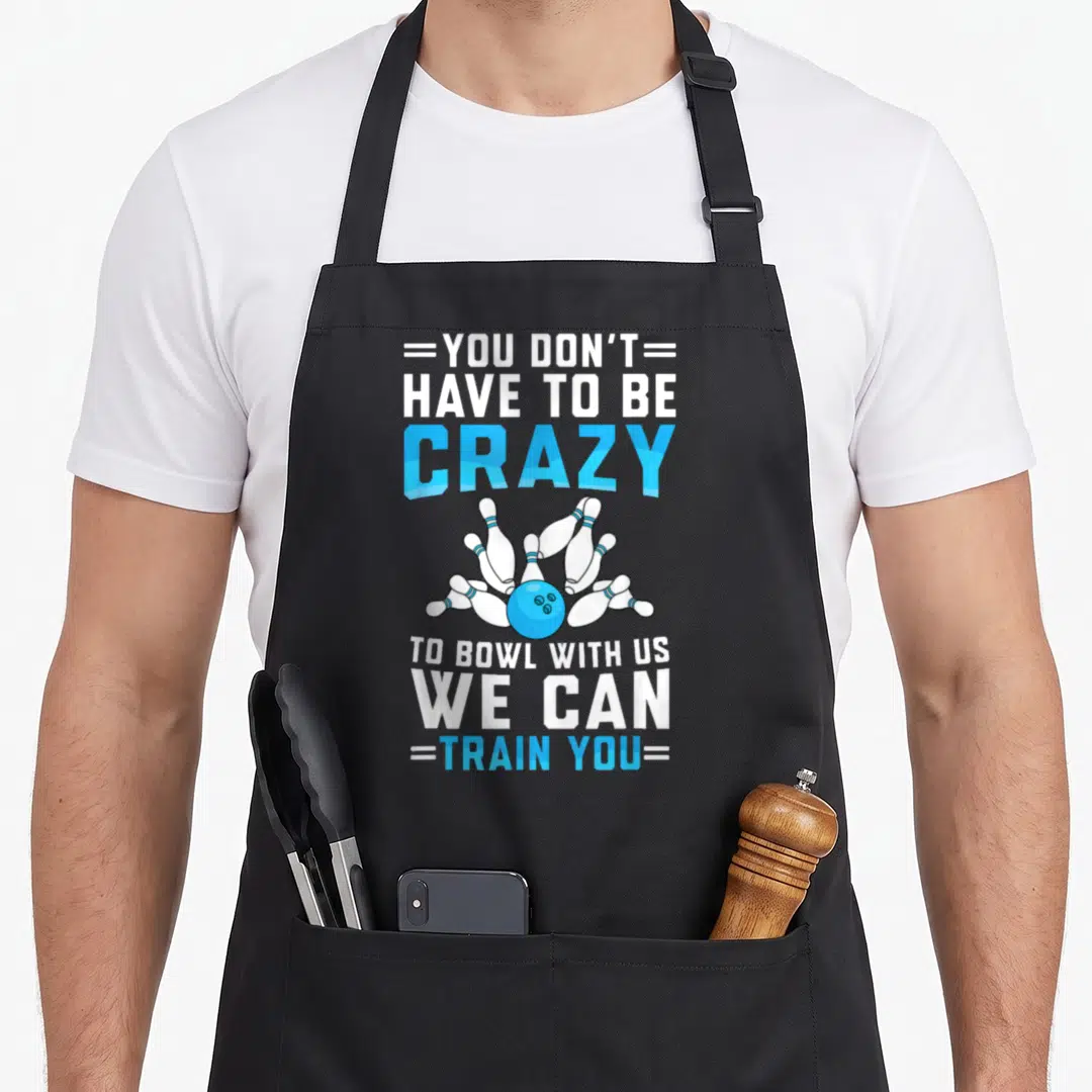Funny bowler bowling player apron - Blue bowling ball knocking over six white pins with You Don't Have To Be Crazy text — shown on a black cotton canvas apron against a white background