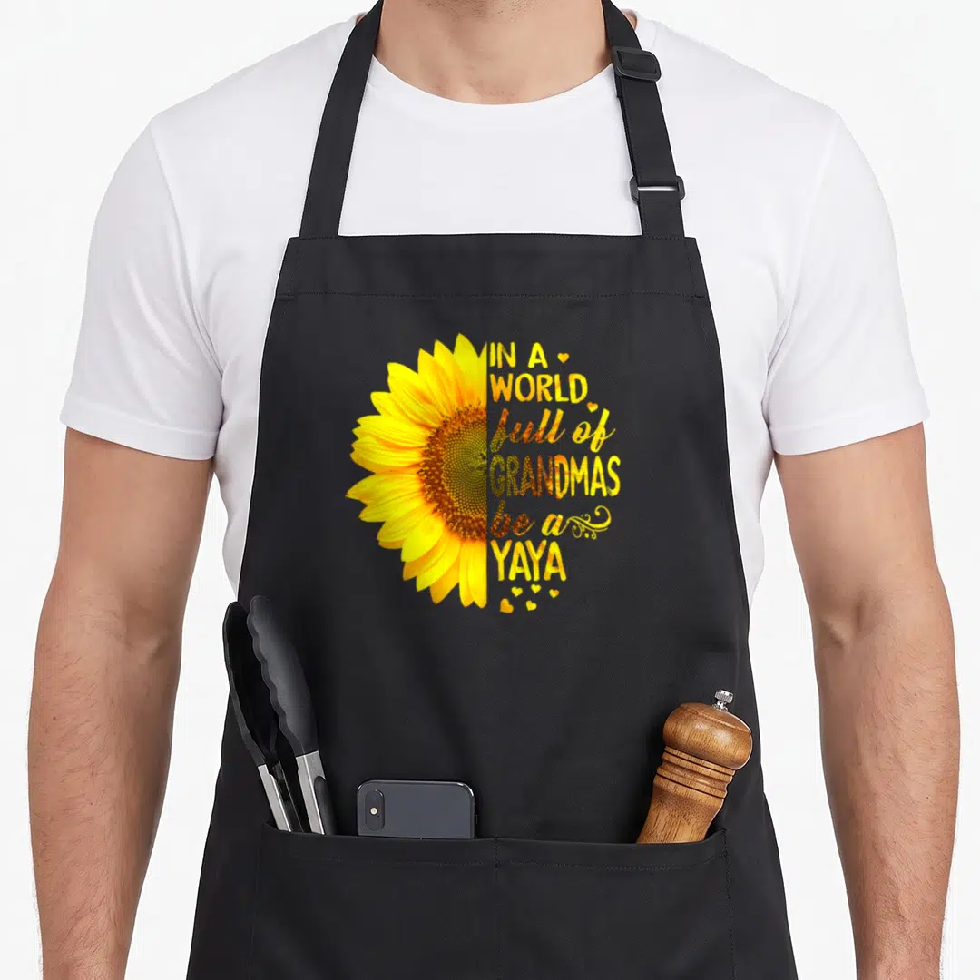 Yaya grandma's aprons - Yellow sunflower half-circle with brown center and IN A WORLD full of GRANDMAS be a YAYA — shown on a black cotton canvas apron against a white background