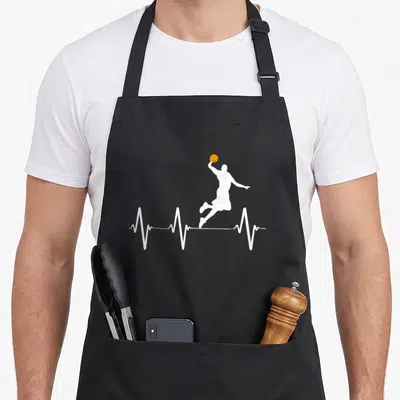 Heartbeat basketball apron - White jumping player silhouette and orange basketball on a white heartbeat line — shown on a black cotton canvas apron against a white background