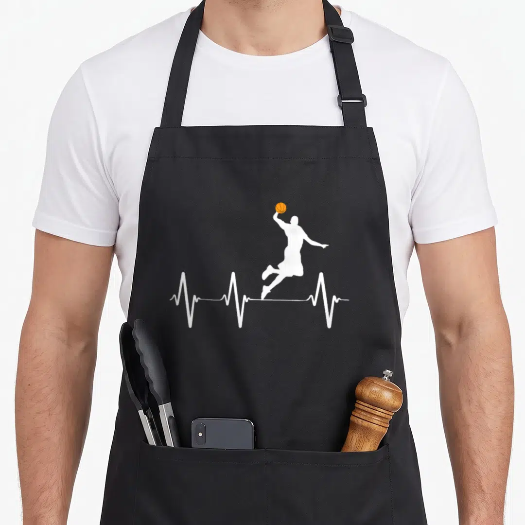 Heartbeat basketball apron - White jumping player silhouette and orange basketball on a white heartbeat line — shown on a black cotton canvas apron against a white background