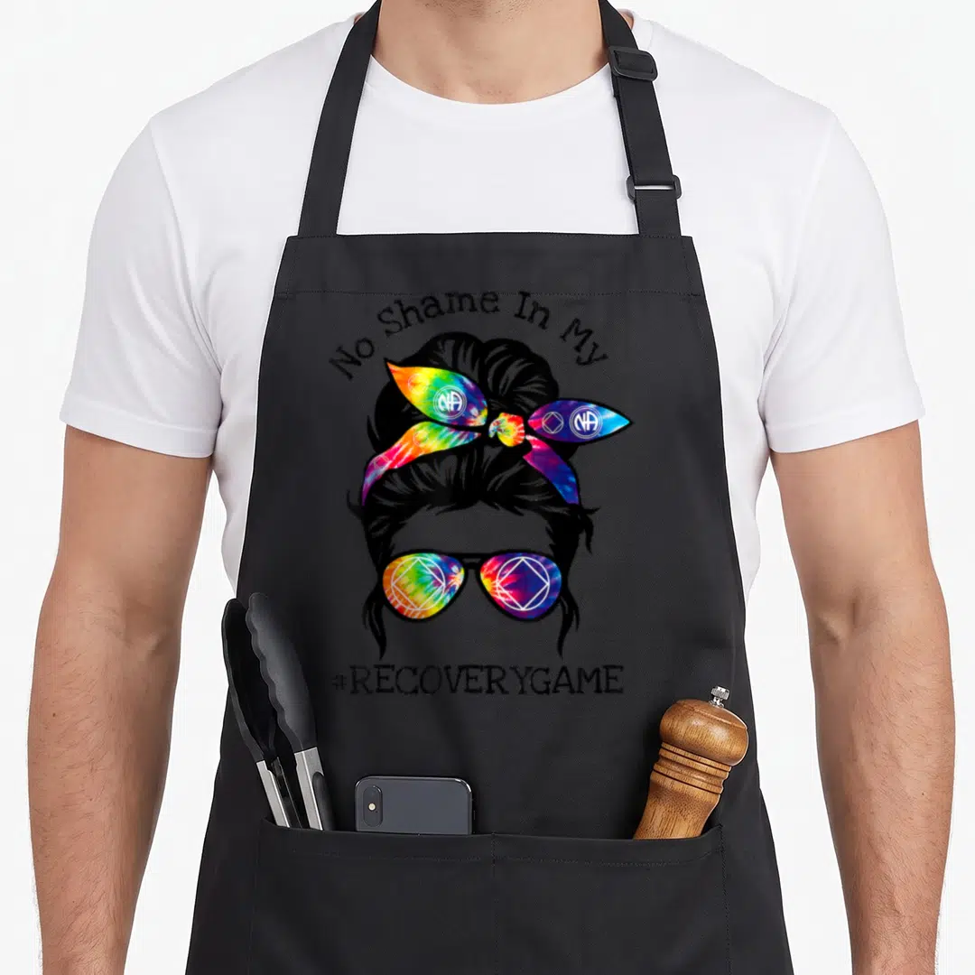 Narcotic sobriety apron - Woman silhouette with rainbow tie-dye headband and sunglasses under No Shame In My text — shown on a black cotton canvas apron against a white background