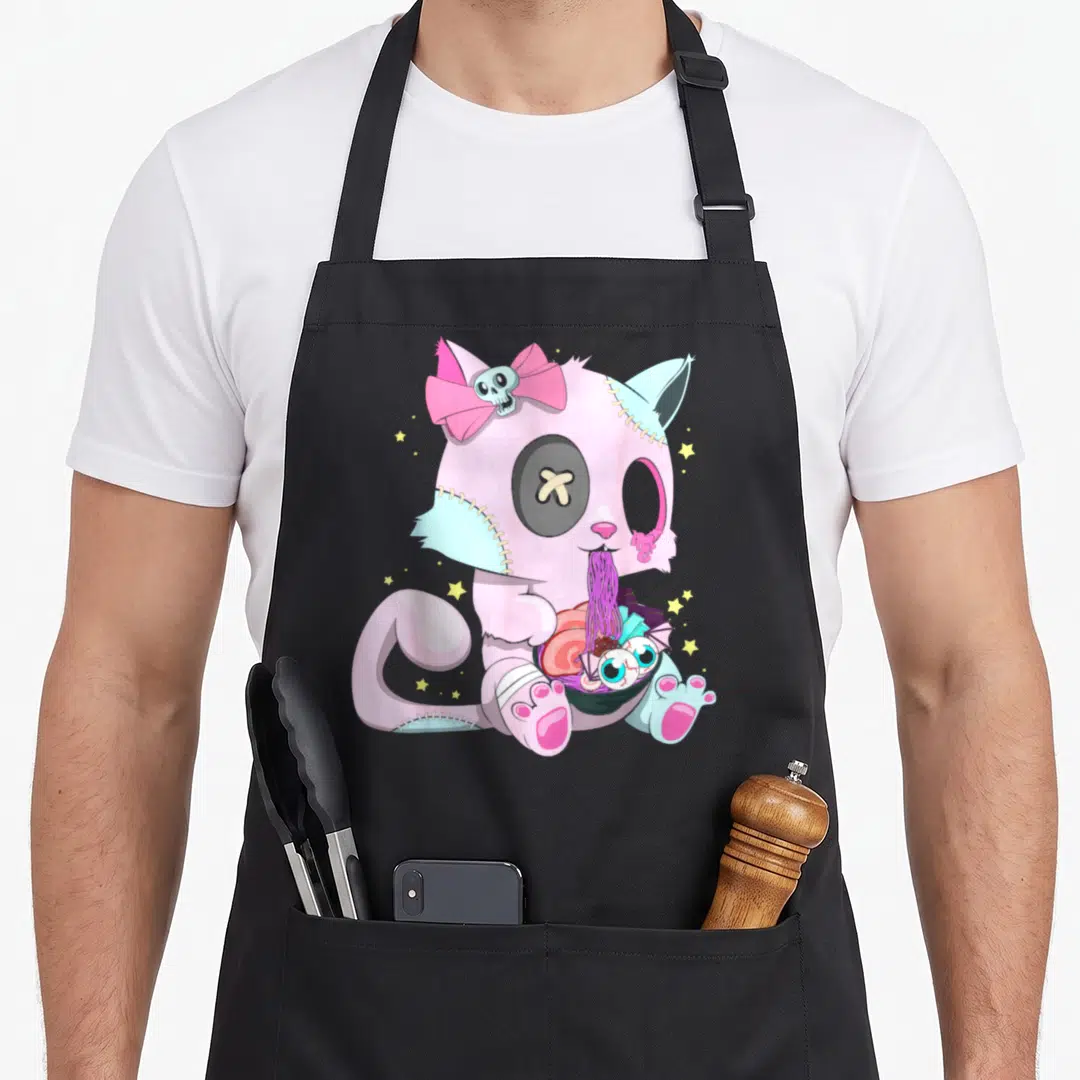 Witchy cat apron - Pink stitched cat holding purple ramen bowl with eyeballs and skull bow — shown on a black cotton canvas apron against a white background
