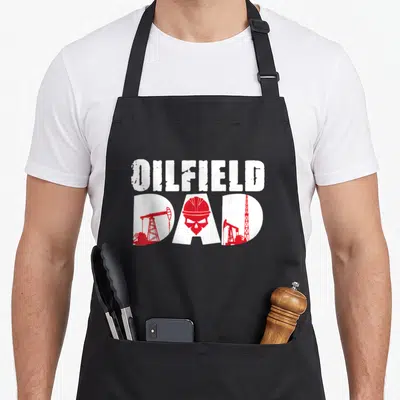 Oilfield father day apron - Distressed OILFIELD DAD text with red oil pumps and skull in hard hat on black background — shown on a black cotton canvas apron against a white background