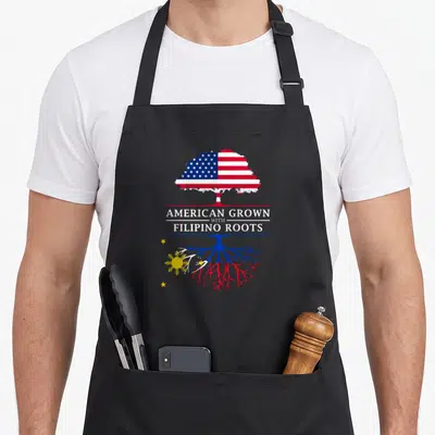 Grown filipino american apron - Tree graphic with US flag canopy and Philippine flag roots separated by white text — shown on a black cotton canvas apron against a white background